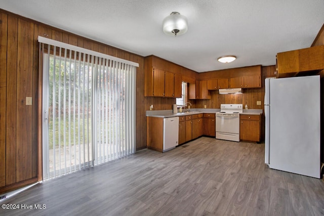 kitchen featuring a textured ceiling, white appliances, wooden walls, and light hardwood / wood-style flooring