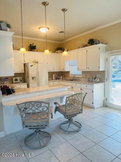 kitchen featuring a kitchen bar, white cabinetry, white fridge with ice dispenser, and decorative light fixtures