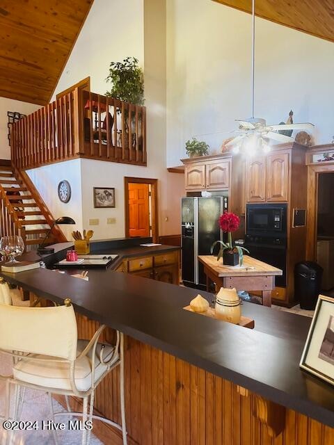 kitchen with kitchen peninsula, black appliances, high vaulted ceiling, ceiling fan, and a breakfast bar