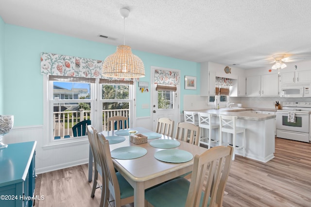 dining space with a textured ceiling, light wood-type flooring, sink, and ceiling fan with notable chandelier