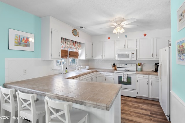 kitchen with white appliances, dark hardwood / wood-style floors, white cabinets, kitchen peninsula, and ceiling fan