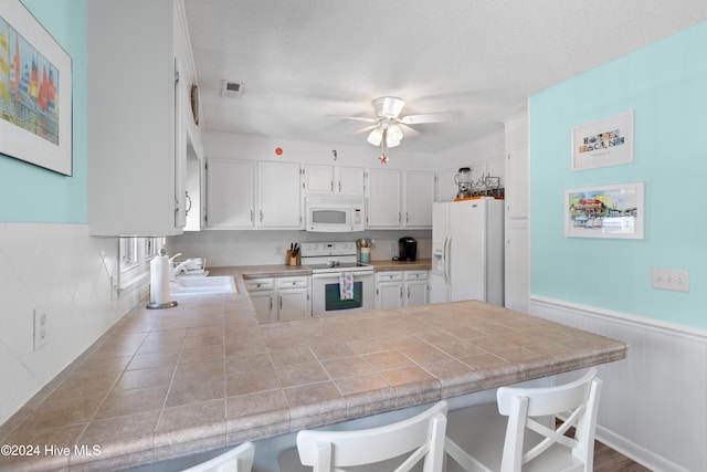 kitchen with white cabinetry, kitchen peninsula, white appliances, and a kitchen bar