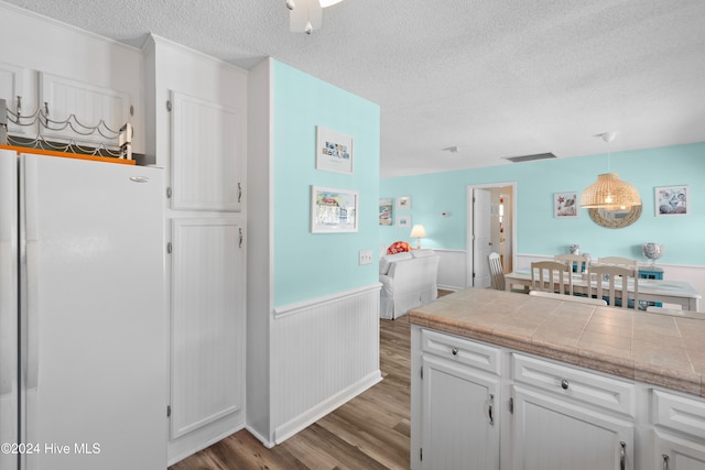 kitchen with light hardwood / wood-style floors, white cabinets, a textured ceiling, white fridge, and decorative light fixtures