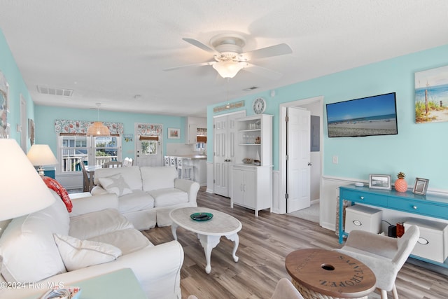 living room featuring a textured ceiling, light hardwood / wood-style floors, and ceiling fan