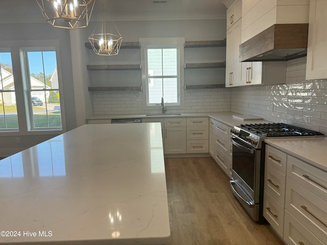 kitchen featuring gas stove, light stone countertops, custom exhaust hood, white cabinets, and pendant lighting