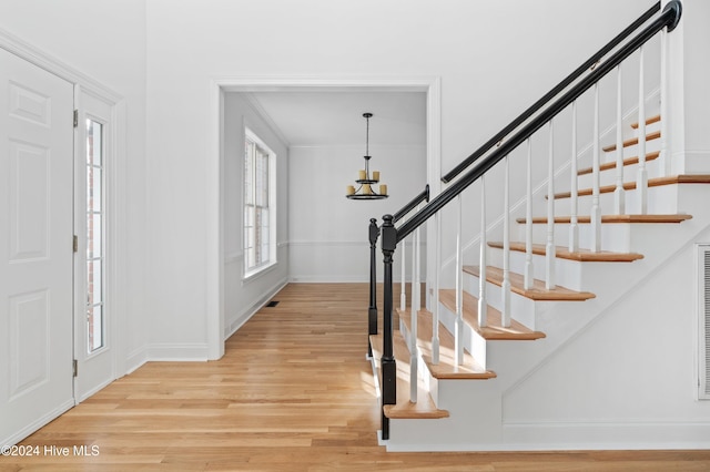 foyer with light wood-type flooring, crown molding, and an inviting chandelier