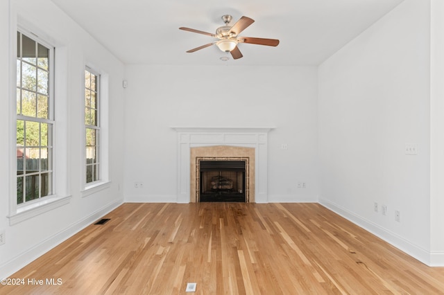 unfurnished living room with ceiling fan, a tile fireplace, and light hardwood / wood-style flooring