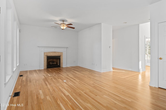 unfurnished living room with light wood-type flooring, ceiling fan, and a tiled fireplace