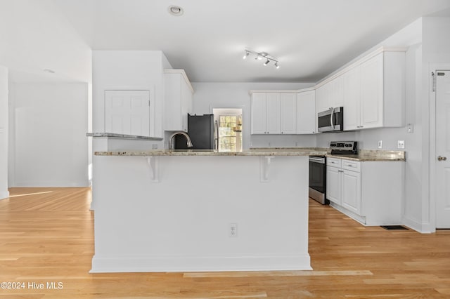 kitchen with light stone countertops, light hardwood / wood-style flooring, white cabinets, and appliances with stainless steel finishes