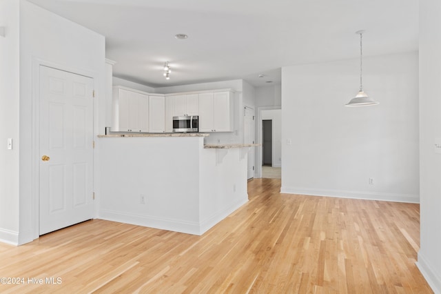 kitchen with white cabinetry, hanging light fixtures, light hardwood / wood-style flooring, kitchen peninsula, and a breakfast bar