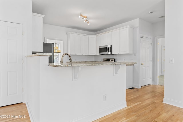 kitchen featuring white cabinets, a kitchen breakfast bar, stainless steel appliances, and light hardwood / wood-style flooring