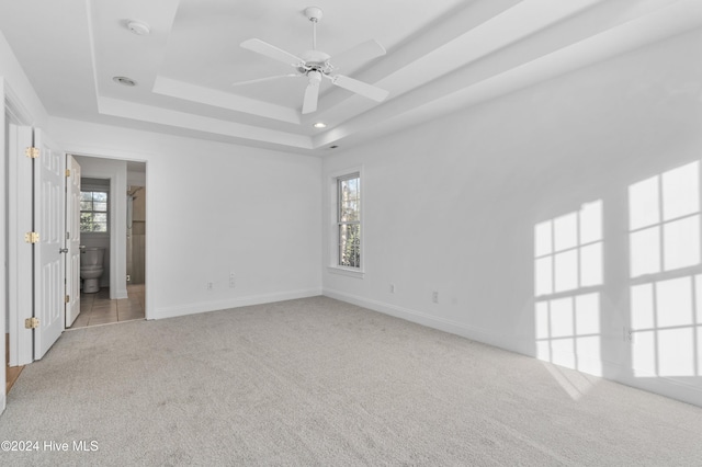 carpeted spare room featuring a tray ceiling and ceiling fan