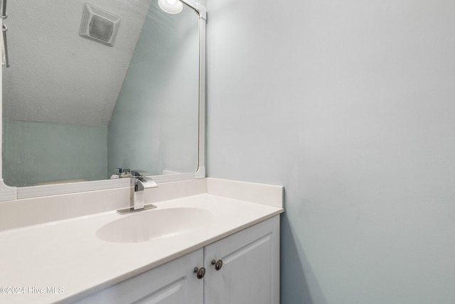 bathroom featuring vanity, vaulted ceiling, and a textured ceiling