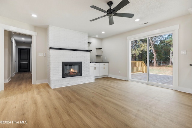 unfurnished living room with a brick fireplace, a textured ceiling, light hardwood / wood-style flooring, and ceiling fan