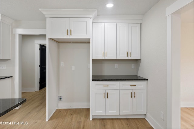 kitchen with white cabinetry, light hardwood / wood-style flooring, and dark stone countertops