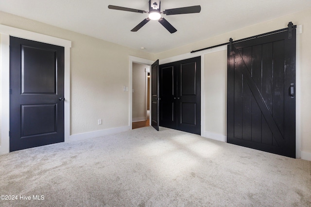 unfurnished bedroom featuring carpet, ceiling fan, and a barn door