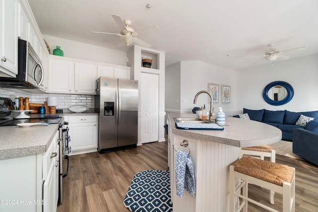 kitchen with dark hardwood / wood-style flooring, a center island with sink, sink, white cabinetry, and appliances with stainless steel finishes