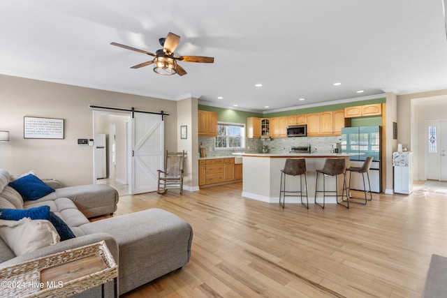 living room with light wood-type flooring, a barn door, ceiling fan, and crown molding