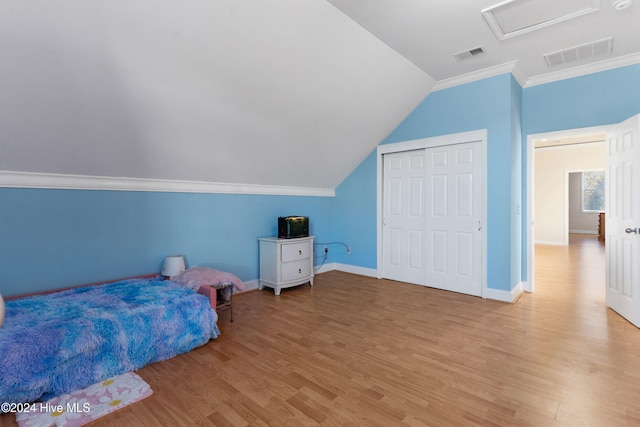 bedroom with light wood-type flooring, lofted ceiling, crown molding, and a closet