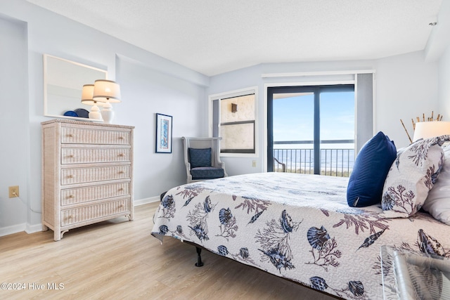 bedroom with access to exterior, a textured ceiling, baseboards, and wood finished floors