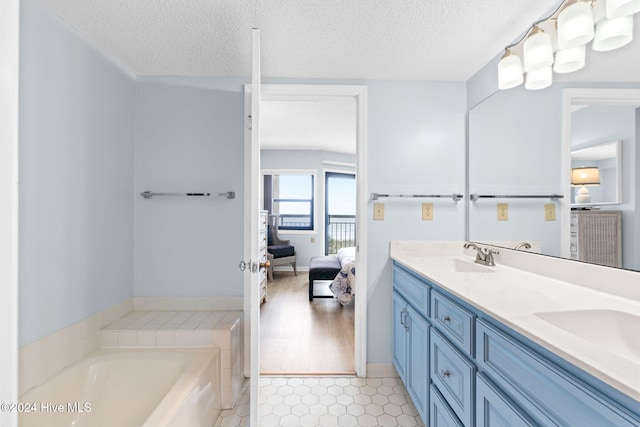 bathroom with connected bathroom, a garden tub, a sink, and a textured ceiling