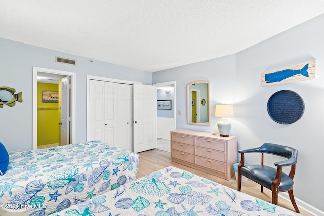 bedroom with a closet, visible vents, light wood-style floors, a textured ceiling, and baseboards