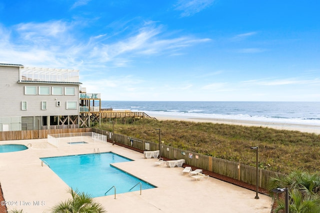 community pool featuring a water view, fence, a view of the beach, and a patio