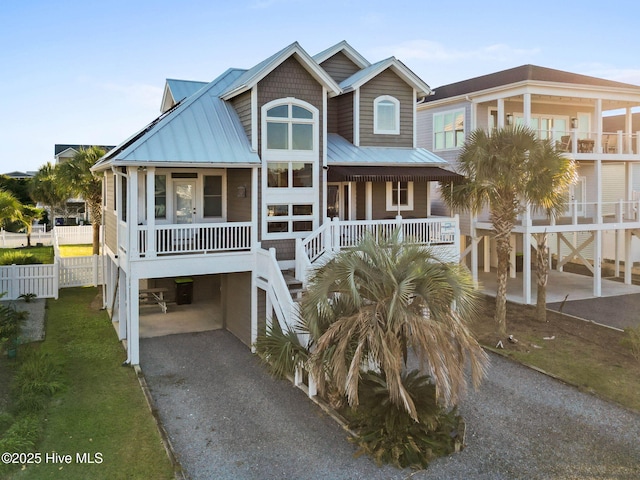 coastal home with gravel driveway, covered porch, metal roof, and a carport