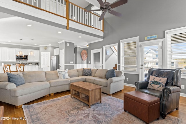 living area featuring baseboards, ceiling fan, ornamental molding, a high ceiling, and light wood-type flooring