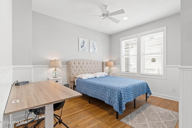 bedroom with a ceiling fan, wood finished floors, and wainscoting