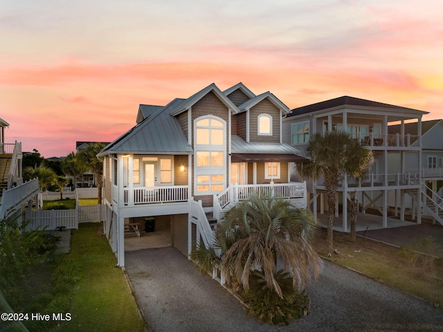 coastal home with driveway, stairway, metal roof, a porch, and a carport