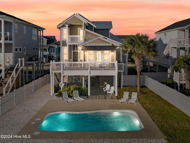 back house at dusk with a fenced in pool, a patio, and a balcony