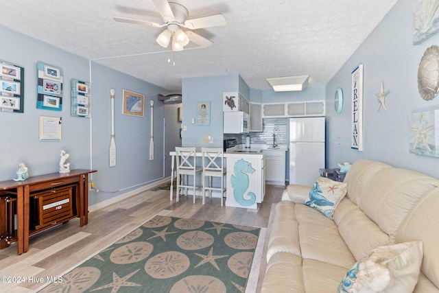 living room featuring a textured ceiling, light hardwood / wood-style floors, ceiling fan, and sink