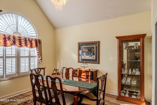 dining area with a notable chandelier, wood-type flooring, and lofted ceiling