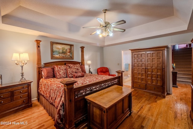 bedroom featuring light wood-type flooring, a tray ceiling, ceiling fan, and ensuite bathroom