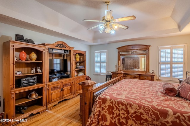 bedroom with light hardwood / wood-style floors, a raised ceiling, and ceiling fan