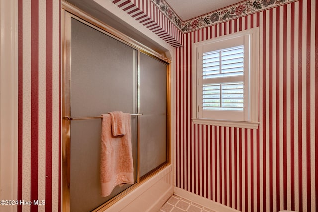 bathroom featuring combined bath / shower with glass door and a textured ceiling