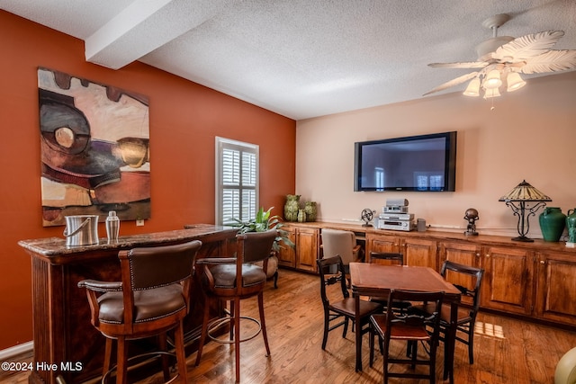 dining room featuring bar area, ceiling fan, a textured ceiling, and light hardwood / wood-style flooring