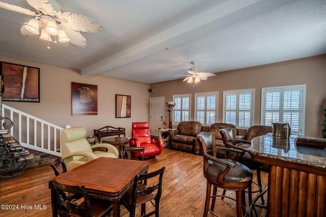 dining room featuring ceiling fan, beamed ceiling, wood-type flooring, and a textured ceiling