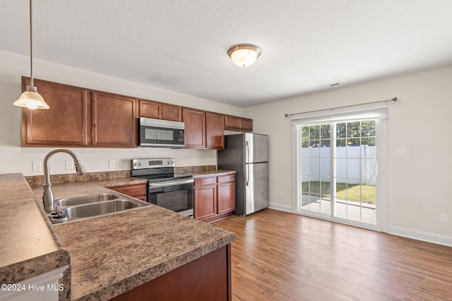 kitchen with sink, hardwood / wood-style floors, decorative light fixtures, and appliances with stainless steel finishes