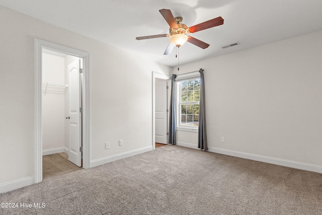 unfurnished bedroom with a closet, light colored carpet, a spacious closet, and ceiling fan