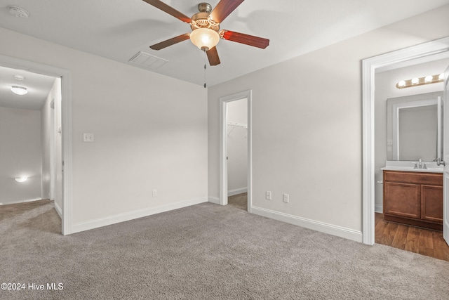 unfurnished bedroom with carpet flooring, connected bathroom, ceiling fan, sink, and a walk in closet