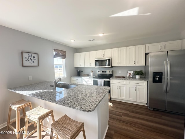 kitchen featuring a kitchen breakfast bar, appliances with stainless steel finishes, a sink, and white cabinets