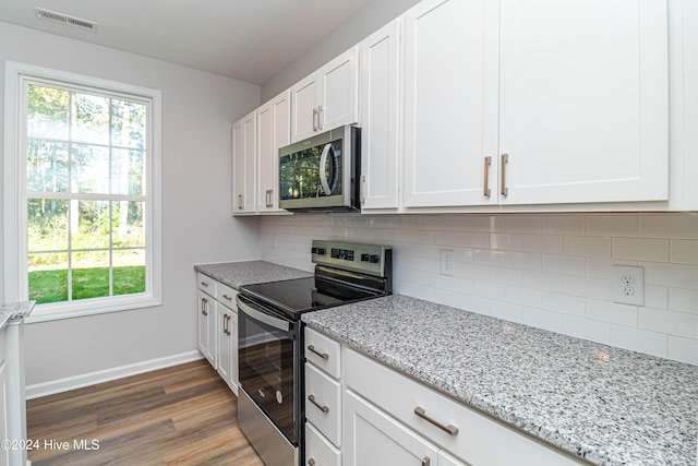 kitchen with dark wood-type flooring, appliances with stainless steel finishes, white cabinetry, light stone countertops, and decorative backsplash