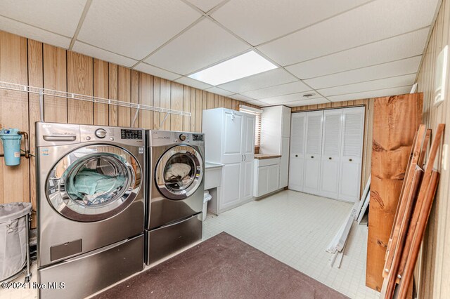 clothes washing area with cabinets, wood walls, and washing machine and dryer