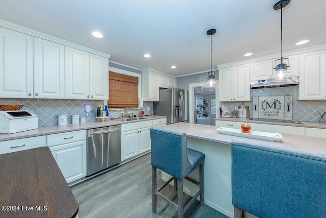 kitchen featuring white cabinets, appliances with stainless steel finishes, light wood-type flooring, and decorative light fixtures