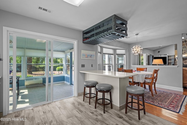 kitchen featuring wood finished floors, a chandelier, a kitchen breakfast bar, hanging light fixtures, and baseboards