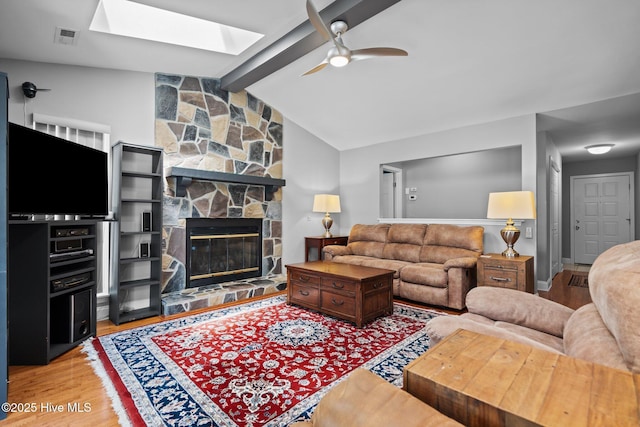 living area featuring ceiling fan, a skylight, wood finished floors, and a fireplace