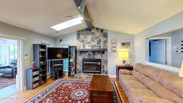 living room featuring ceiling fan, wood-type flooring, a fireplace, and lofted ceiling with skylight