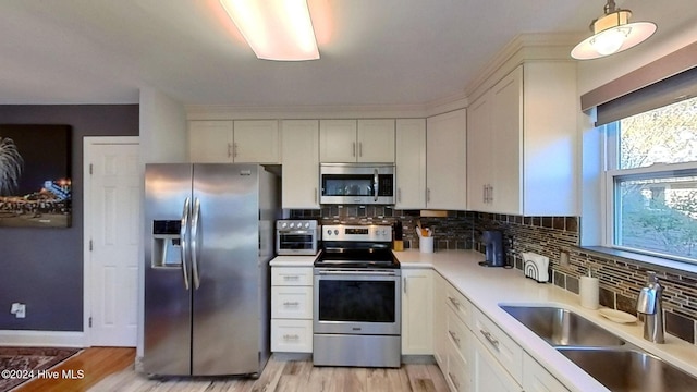 kitchen featuring white cabinetry, stainless steel appliances, decorative light fixtures, and sink